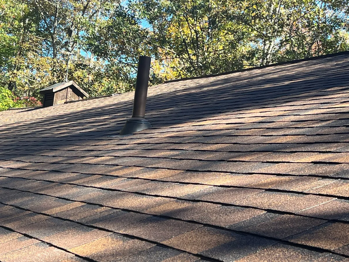 Black metal flue rising through a new boot, shingles running up to the ridge behind it