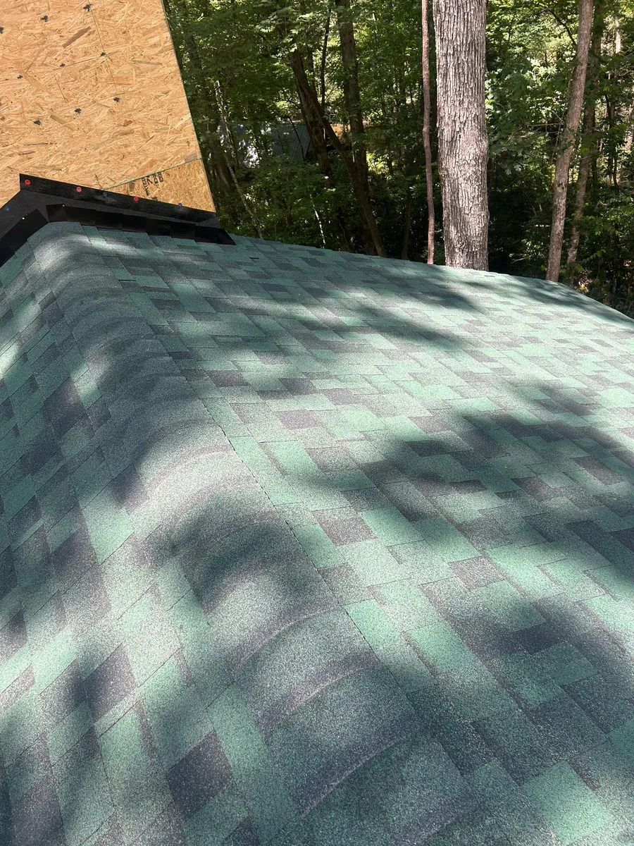 Gable run of green shingles with tree shadows falling across the new course lines