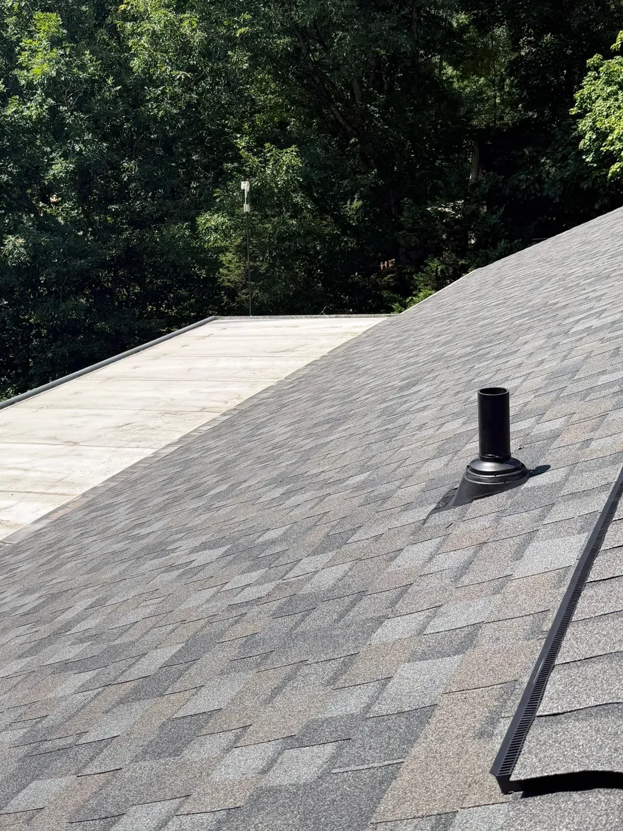 Black pipe boot sealed into the shingle field, ridge vent above and a low-slope section alongside