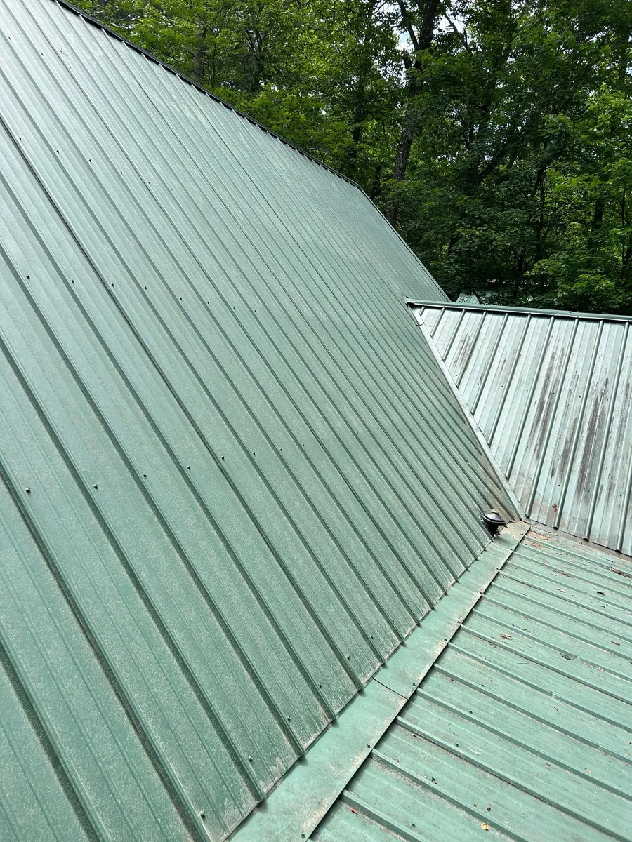 Green metal roof where two slopes meet at a ridge, panel ribs running to the eave