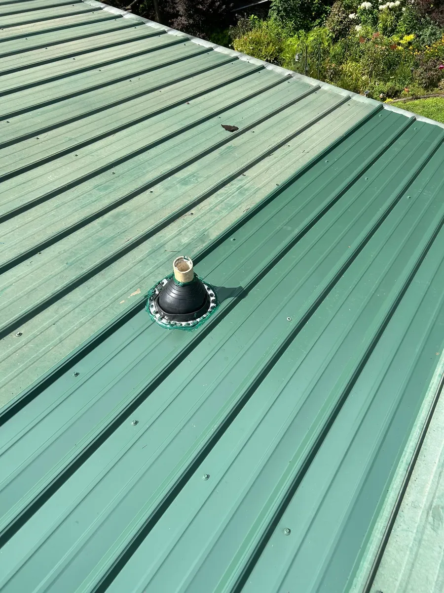 New black pipe boot flashed into a green standing-seam metal roof, sealant fresh around the collar