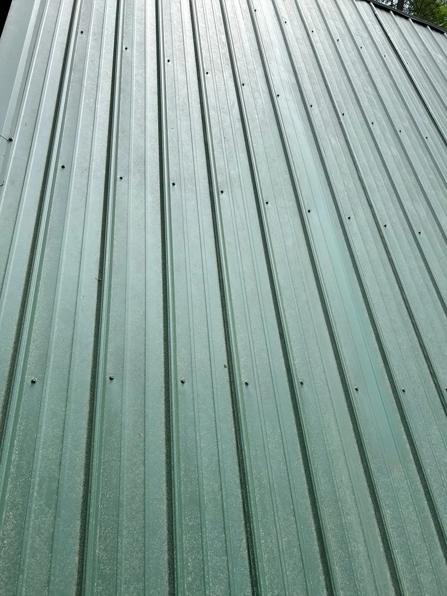 Close view along the ribs of a green standing-seam panel run, fasteners set in line